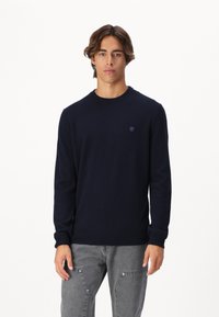 Granatowy sweter crewneck wykonany z miękkiego materiału, z długimi rękawami; z detalem logo na klatce piersiowej oraz prążkowanymi mankietami i dolnym brzegiem.