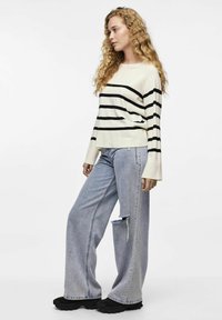 Kremstripet genser med svarte striper, vide ermer, kombinert med lyseblå vide jeans med hull. Svart sko fullfører antrekket.