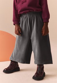 Pantaloni largi din corduroy gri, cu cintura elastică, asociați cu cizme de gleznă lucioase, de culoare burgundă, cu fermoar lateral.