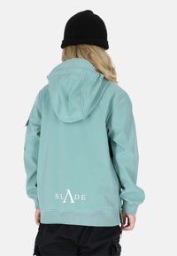 Mintgrüne Kapuzenjacke mit einem schwarzen Logo auf dem Rücken, mit glatter Oberfläche, gerippten Manschetten und mit Reißverschlüssen versehenen Taschen.