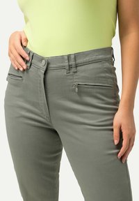 Ljusgrön stickad topp tillsammans med grå slim-fit byxor med framdragkedjor, bältesöglor och en slät yta.