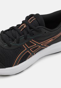 Svart sportsko med mesh-overdel, oransje detaljer og en hvit såle. Har lisser og karakteristiske sidedesignelementer.