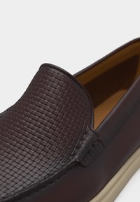 Mocassin pour homme marron foncé à enfiler avec dessus texturé et côtés en cuir lisse, intérieur beige et semelle de couleur claire.