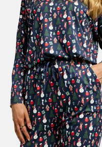 Sötétkék pizsama szett, amely egész felületén élénk színekben havas manók, karácsonyfák és ünnepi motívumok láthatók, rugalmas derékpánttal.