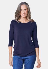 Navyblaues Top mit Dreiviertelärmeln und Rundhalsausschnitt. Aus weichem, dehnbarem Stoff in lockerer Passform, kombiniert mit Jeans.