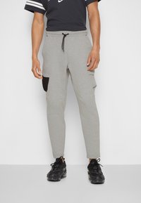 Šedé joggers vyrobené z měkké látky, s tapered designem, elastickým pasem s šňůrkou a černou boční kapsou.