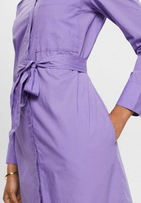 Lavendelfärgad knapp-up klänning med långa ärmar, knytning i midjan och sidofickor. Slät bomullstyg med en avslappnad, figurnära design.