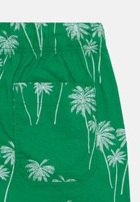 Gröna shorts med ett palmträdsmönster i vitt, med en bakficka och resårmidja för komfort. Materialet är lättviktigt bomull.
