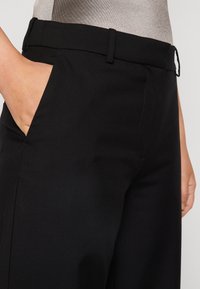 Czarne spodnie o dopasowanym kroju, wykonane z gładkiego materiału, z dopasowanym paskiem w talii, kieszeniami bocznymi i prostą, czystą sylwetką nogawki.