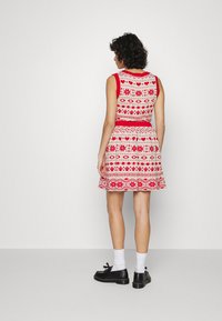 Vestido estampado vermelho e branco com design sem mangas, saia rodada e motivos decorativos. Sapatos pretos e meias brancas completam o visual.