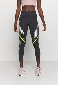 Svarta sportleggings med hög midja, med vita och neon gula diagonala ränder längs sidorna. Slät, elastisk tyg.