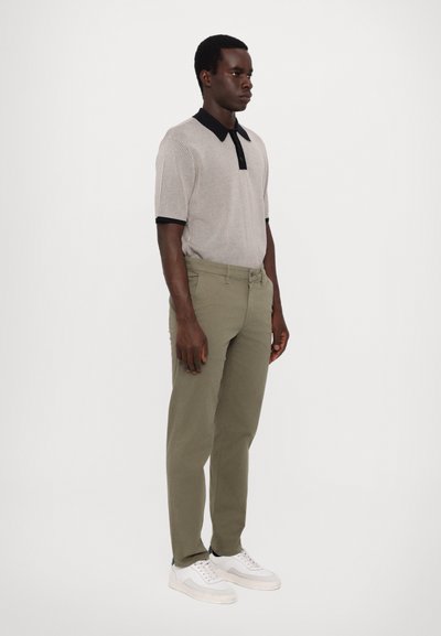 Stripet kortermet polo skjorte i beige og svart med krage, parret med olivengrønne chinos og hvite joggesko, stående posisjon.