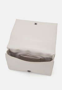 Beżowa skórzana torba na ramię o gładkiej fakturze, z zapięciem na magnes oraz wewnętrzną kieszenią wyembosowaną napisem "Calvin Klein".