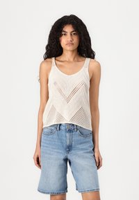 Light beige knit tank top with a chevron pattern and open weave, paired with light blue denim shorts.