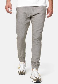 Pantaloni jogger grigi chiari con polsini elasticizzati, realizzati in un tessuto testurizzato e con una vestibilità classica. Abbinati a scarpe da ginnastica bianche e grigie.