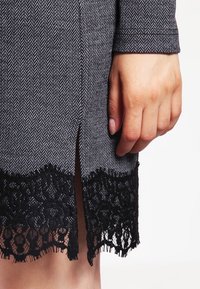 Sukienka w wzór houndstooth z czarnym koronkowym dołem, z bocznym rozcięciem. Ma miękką teksturę i dopasowany krój.