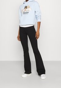 Vaaleansininen huppari, jossa on kukkakuvio ja "Fiorucci"-teksti, yhdistetty mustiin leveisiin farkkuihin ja valkoisiin tennareihin. Rentoa istuvuutta, puuvillasta valmistettu.