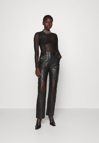 Μαύρο δερμάτινο παντελόνι με λεπτομέρειες κοπής, ψηλή μέση και ίσια γραμμή. Συνδυάζεται με μια διάφανη μαύρη μπλούζα από διχτυωτό υλικό και χοντρή ασημένια αλυσίδα.