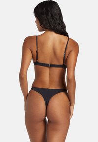 Černé bikiny s tenkými nastavovacími ramínky a minimalistickým designem, s nízkým vystřižením a měkkou, hladkou texturou látky.