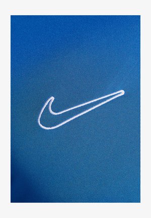 Nike-Sportbekleidung aus lebhaft blauem Stoff mit feiner Textur; auffälliges, weißes gesticktes Swoosh-Logo. Nahaufnahme zeigt die Materialqualität.