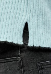 Haut en maille côtelée bleu clair avec une petite découpe à l'ourlet, associé à un jean denim noir avec un bouton argenté et des coutures visibles.