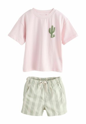 Rožnata majica s kratkimi rokavi z zelenim motivom kaktusa, združena z lahkimi bež kratkimi hlačami z navpičnimi črtami in vrvico za pritrjevanje, primerna za priložnostno nošenje.