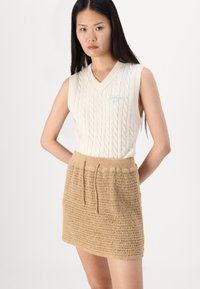 Strikket ermeløs genser i off-white med v-hals og blå broderi, sammen med et lyst heklet miniskjørt med snor i livet.