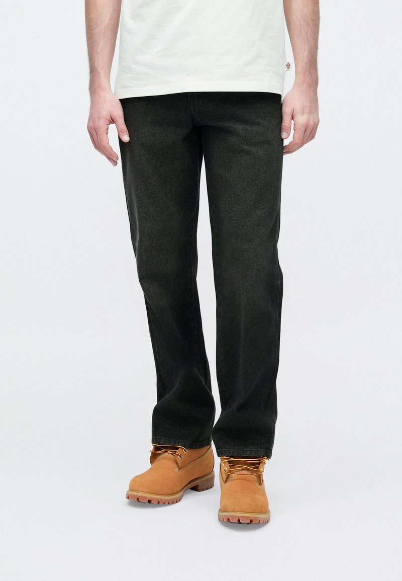 Jean noir à coupe droite avec une texture douce, porté avec des bottes en cuir marron clair dotées d'une semelle robuste et de détails à lacets.