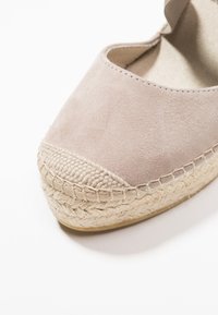 Světle růžové semišové espadrilky s tkanou jutu jako podrážkou, kulatou špičkou a švy podél okrajů. Texturovaný povrch a klasický design.