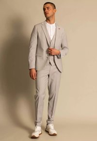 Lichtgrijs driedelig pak met een slim fit, gestructureerde stof en bijpassende broek. Witte shirt eronder, gecombineerd met witte sneakers.