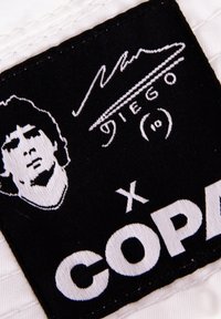 Zwarte stoffen label met een witte geborduurde portret, handtekening en tekst "DIEGO" en "COPA," met een sportief ontwerp.