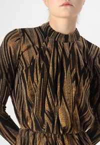 Schwarz-goldenes, gemustertes Langarmkleid mit hohem Kragen und plissierten Details, das aus einem strukturierten Stoff mit metallic schimmerndem Finish gefertigt ist.