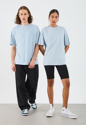 Sky blue oversized t-shirts, black ribbed bike shorts, and casual shoes. Model on left wears dark jeans and sneakers; right wears white sneakers.