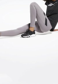 Šedé sportovní legíny s texturovanými panely, v kombinaci s černými teniskami. Vrchní část je černá s logem na hrudi.