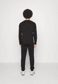 Musta pitkähihainen paita ja siihen kuuluvat housut, jotka on valmistettu sileästä kankaasta. Asu on muotoiltu tiiviisti ja se on yhdistetty valkoisiin urheilu kenkiin.