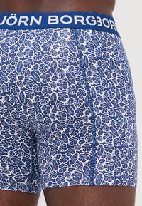Boxers en coton à motifs floraux bleus sur un fond blanc. Dotés d'une ceinture bleue avec le logo "BJÖRN BORG". Fabriqués en tissu doux.
