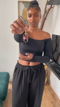 Gold-tone ladybug charm pendant with red and black enamel, detailed with accents. Model displaying the pendant in a bright indoor setting.