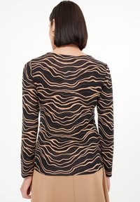 Long-sleeve top with a wave pattern in beige and black, made of soft fabric. Features a rounded neckline and a fitted cut.