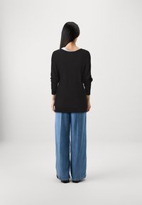 Haut noir à manches longues avec un large décolleté, associé à un jean large bleu clair. Texture lisse, coupe décontractée. Des chaussures noires complètent la tenue.