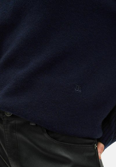 Maglione a maglia blu navy con tessuto testurizzato e polsini a coste, caratterizzato da un piccolo logo in rilievo sulla parte inferiore sinistra. Abbinato a pantaloni in ecopelle nera.