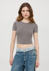 Crop top grigio a coste con maniche corte e scollatura rotonda, abbinato a jeans in denim blu chiaro con taglio irregolare e bordi sfilacciati.