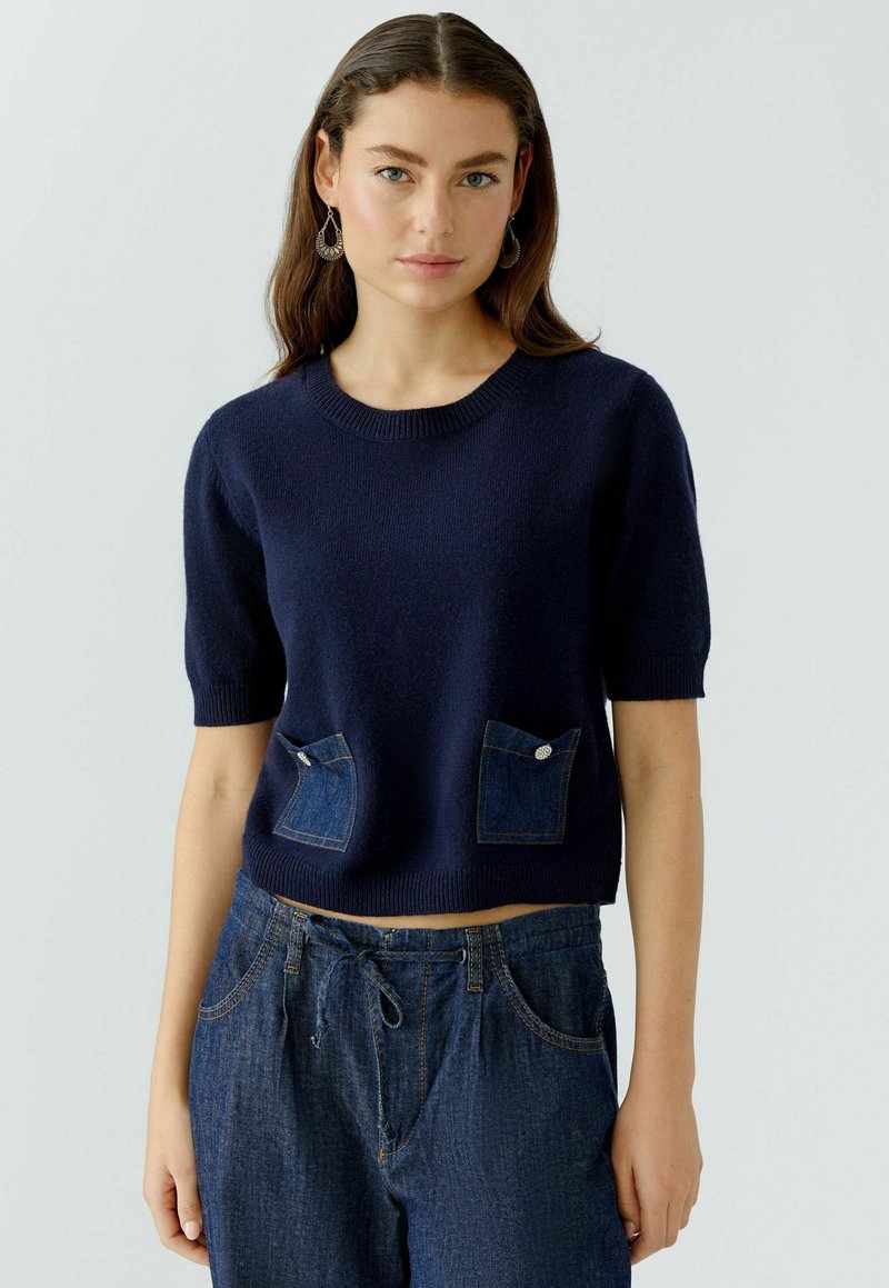 Donkerblauwe short-sleeve trui met een gestructureerde afwerking en twee denim patch pockets. Heeft een ronde halslijn en een relaxed fit.