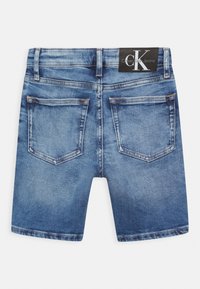 Shorts de denim en un lavados azul medio con diseño de cinco bolsillos, que presentan una etiqueta negra de Calvin Klein Jeans en la cinturilla.