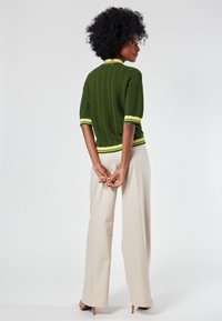 Green ribbed knit top with yellow trim, short sleeves, and a fitted design; paired with beige wide-leg trousers and high-heeled shoes.