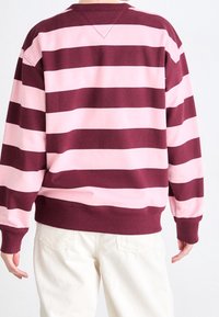 Sudadera a rayas en granate y rosa claro con cuello redondo y puños acanalados, que presenta un ajuste relajado y material de algodón suave.