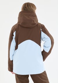 Wasserdichte Jacke mit einem braunen oberen Teil und einem hellblauen unteren Teil, mit Kapuze und glatter Textur. Keine sichtbaren Hardwaredetails.
