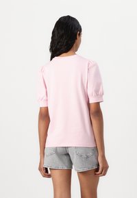Rosa kortärmad t-shirt med puffärmar, rund halsringning och en slät textur, kombinerad med grå denimshorts och en enkel design.