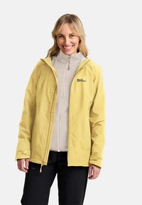Yellow waterproof jacket with a hood, front zipper, and logo; layered over a light gray fleece inner jacket. Black pants.