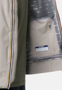 Giacca leggera con esterno beige, zip con dettagli colorati e fodera interna grigia dotata di una tasca per oggetti personali.