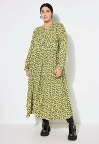Vestido de manga larga con volantes en un brillante amarillo-verde con un estampado de leopardo negro. Terminado con un cuello abotonado y combinado con botas negras gruesas.